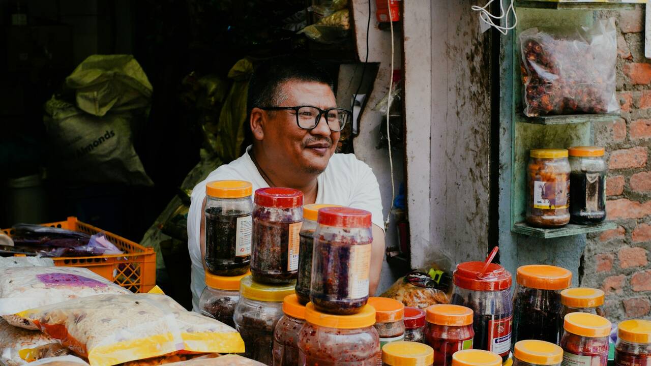 A smiling shopkeeper behind a counter of jars and food products